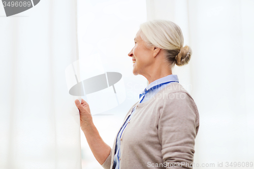 Image of happy senior woman looking through window at home