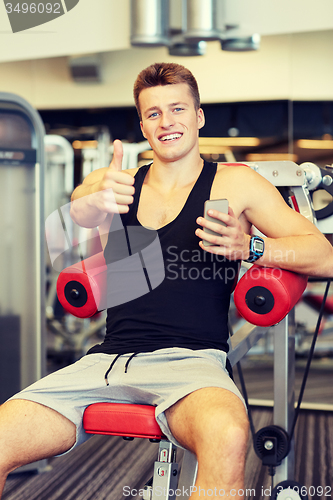 Image of smiling young man with smartphone in gym