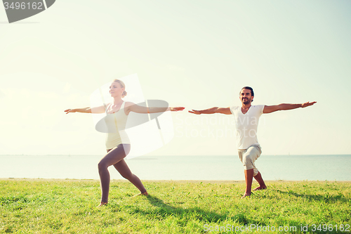 Image of smiling couple making yoga exercises outdoors