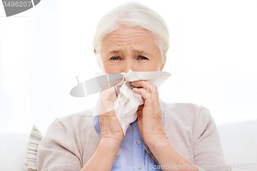 Image of sick senior woman blowing nose to paper napkin