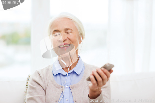 Image of senior woman with smartphone and earphones at home