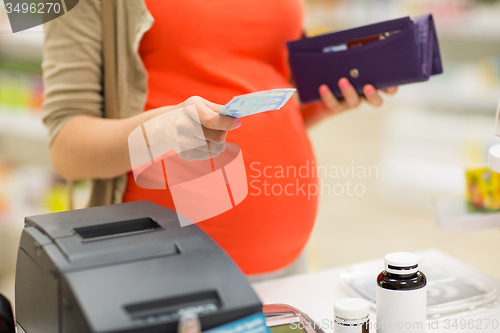 Image of pregnant woman with money at cashbox in drugstore
