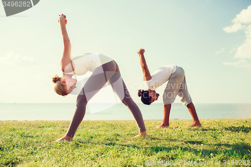 Image of smiling couple making yoga exercises outdoors