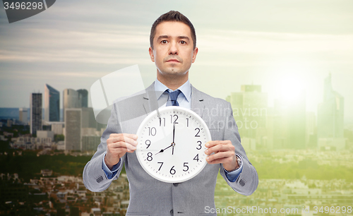 Image of businessman in suit holding clock with 8 o\'clock