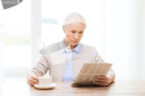 Image of senior woman with coffee reading newspaper at home