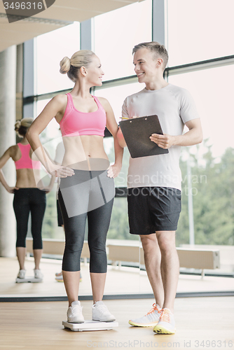 Image of smiling man and woman with scales in gym