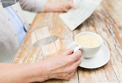 Image of senior woman with coffee reading newspaper at home