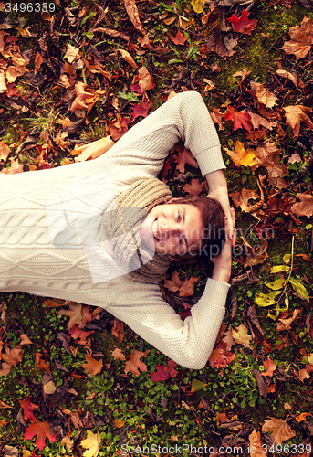 Image of smiling young man lying on ground in autumn park