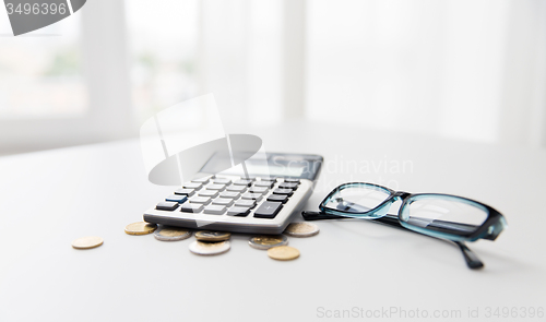 Image of calculator, eyeglasses and coins on office table