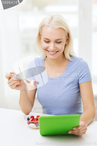 Image of smiling woman eating fruits with tablet pc at home