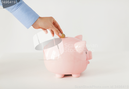 Image of close up of hand putting coin to piggy bank