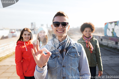 Image of happy teenage friends showing ok sign on street