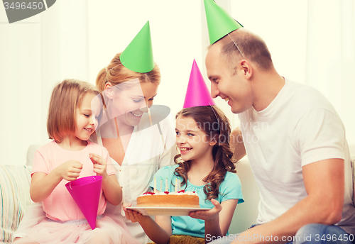 Image of smiling family with two kids in hats with cake