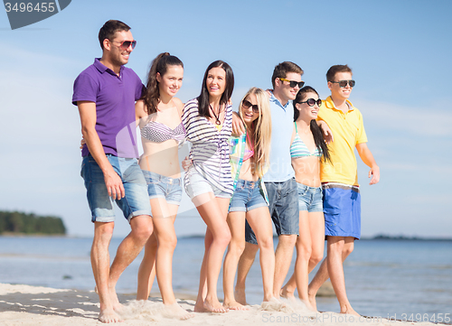 Image of group of happy friends walking along beach