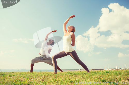 Image of smiling couple making yoga exercises outdoors