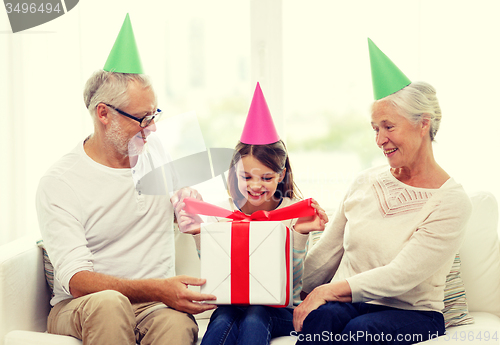 Image of smiling family in party hats with gift box at home