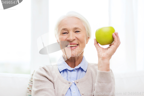 Image of happy senior woman with green apple at home