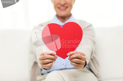 Image of close up of senior woman with red heart at home