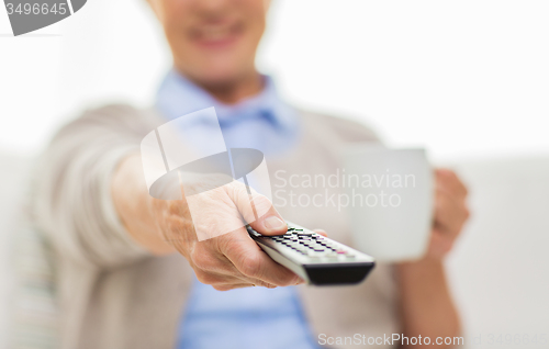 Image of senior woman watching tv and drinking tea at home