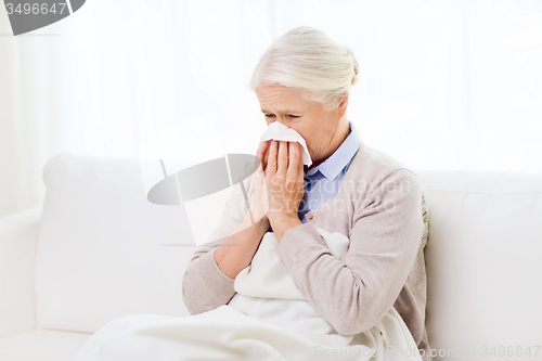 Image of sick senior woman blowing nose to paper napkin