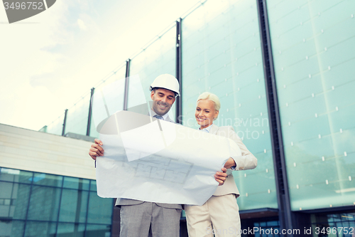 Image of smiling businessmen with blueprint and helmets