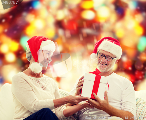 Image of happy senior couple in santa hats with gift box