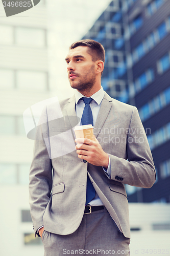 Image of young serious businessman with paper cup outdoors