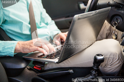 Image of close up of young man with laptop driving car