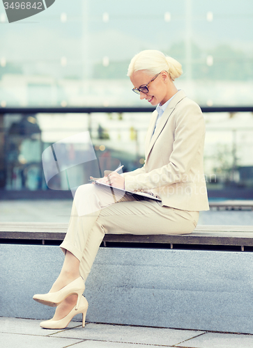 Image of young smiling businesswoman with notepad outdoors