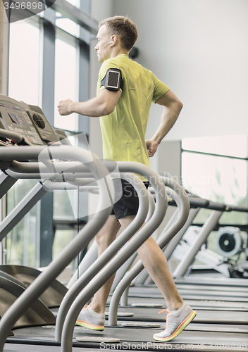 Image of man with smartphone exercising on treadmill in gym