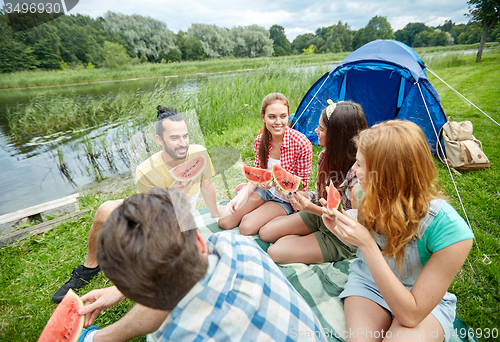 Image of happy friends eating watermelon at camping