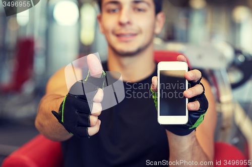 Image of young man with smartphone showing thumbs up in gym