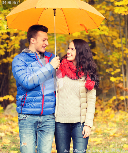 Image of smiling couple with umbrella in autumn park