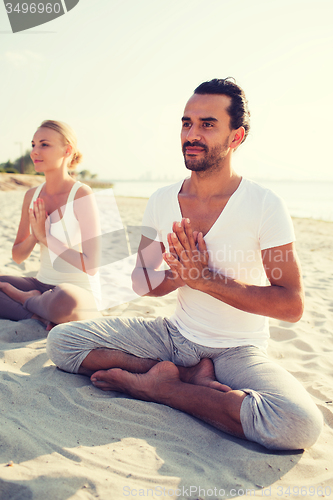 Image of smiling couple making yoga exercises outdoors