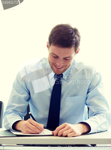 Image of smiling businessman signing papers in office