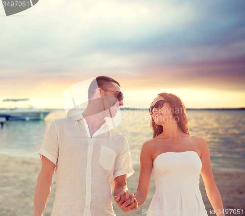 Image of smiling couple in sunglasses walking on beach