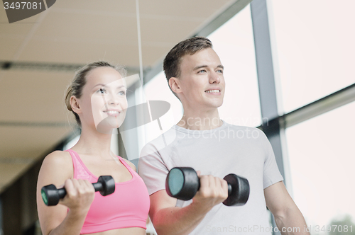 Image of smiling young woman with personal trainer in gym