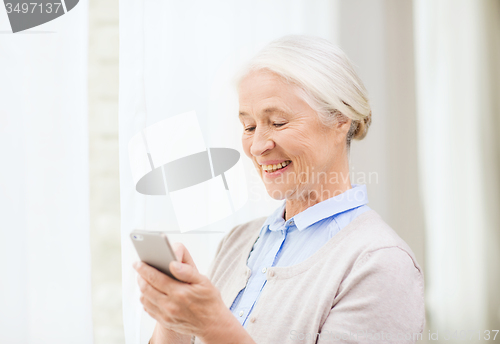 Image of senior woman with smartphone texting at home