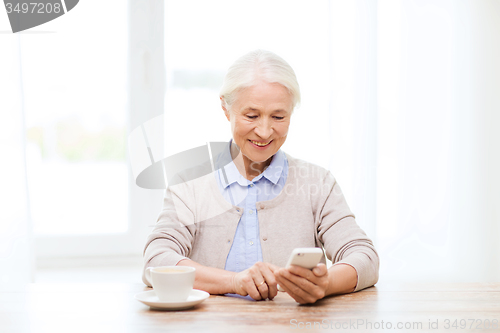 Image of senior woman with smartphone texting at home