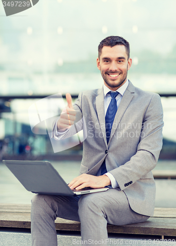 Image of smiling businessman working with laptop outdoors