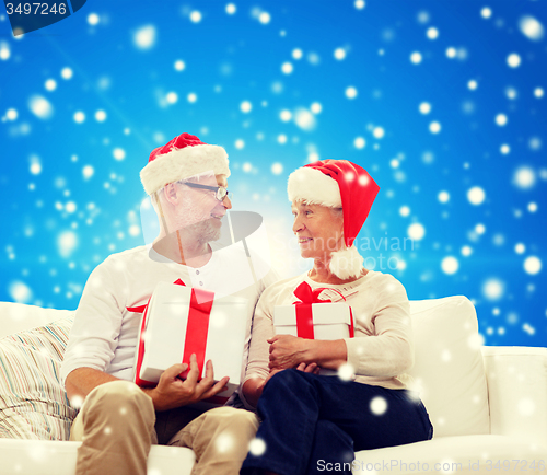 Image of happy senior couple in santa hats with gift boxes