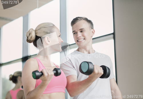 Image of smiling young woman with personal trainer in gym