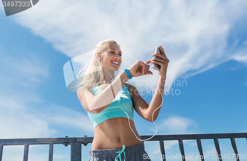 Image of happy woman with smartphone and earphones outdoors