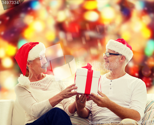 Image of happy senior couple in santa hats with gift box