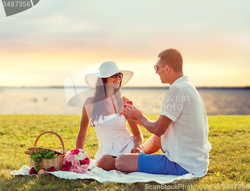 Image of smiling couple with small red gift box on picnic