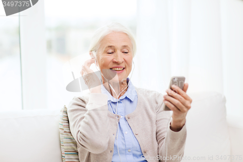 Image of senior woman with smartphone and earphones at home