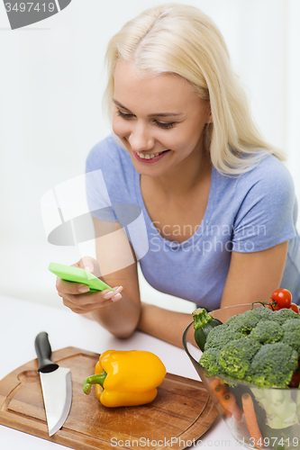 Image of smiling woman with smartphone cooking vegetables