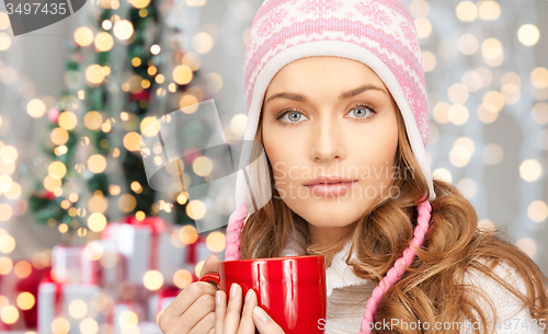 Image of happy young woman in winter hat with cup