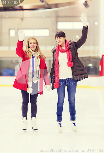 Image of happy girls friends waving hands on skating rink