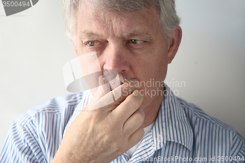 Image of Senior man strokes his mustache.  